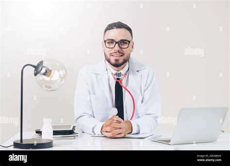 Happy Male Doctor At Office Desk In Hospital Working On Laptop Computer