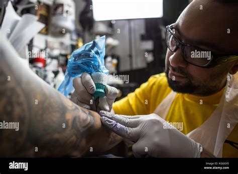 A Tattoo Artist At Worka Tattoo Artist Inks A Designed Onto The Back