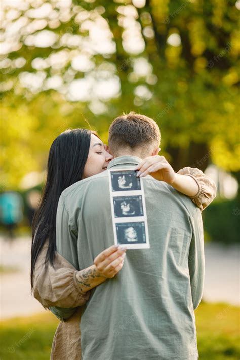 Premium Photo Pregnant Woman And Her Husband Standing In A Park On A Grass And Hugging