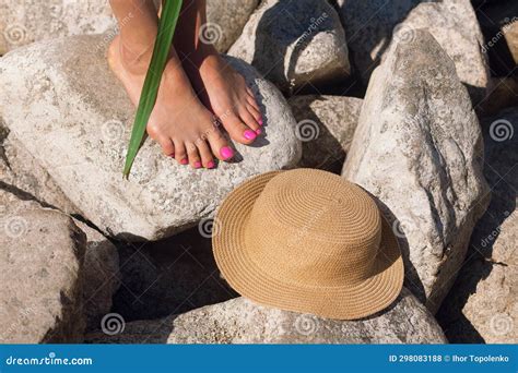 Female Tanned Legs With A Beautiful Pedicure On The Stones Near The