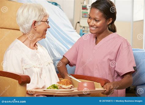 Nurse Serving Meal To Senior Female Patient Sitting In Chair Stock