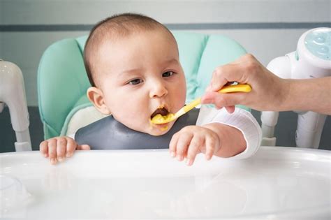 Mamá Alimenta Al Bebé Con Una Cuchara De Puré De Verduras En La Mesa De