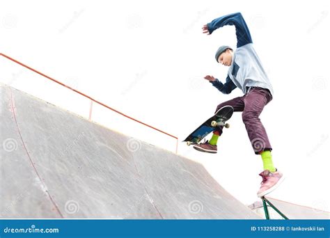 The Teenager Skateboarder In The Cap Does A Trick With A Jump On The