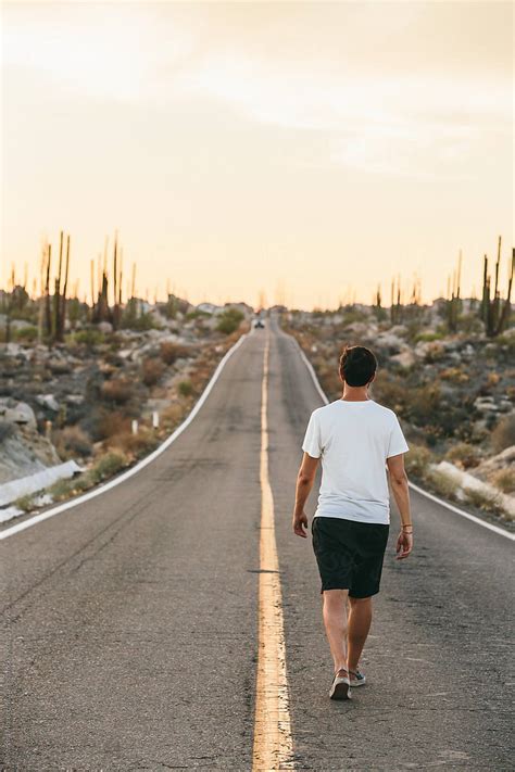 Young Man Walking On A Road In The Desert At Sunset By Stocksy