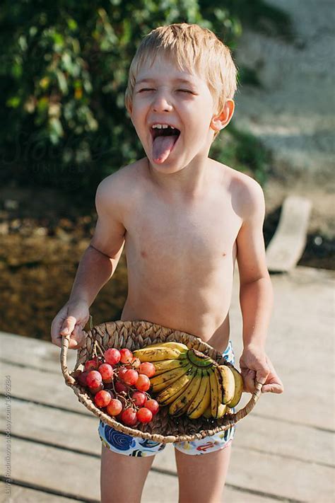 Blond Boy Showing His Tongue And Holding Straw Plate With Fruits