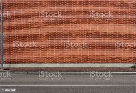 High Brick Wall With A Porphyry Sidewalk And An Asphalt Street In Front
