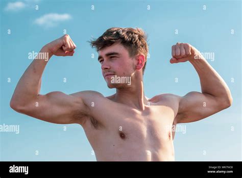 Young Shirtless Muscular Caucasian Man Flexing On A Beach On A Warm