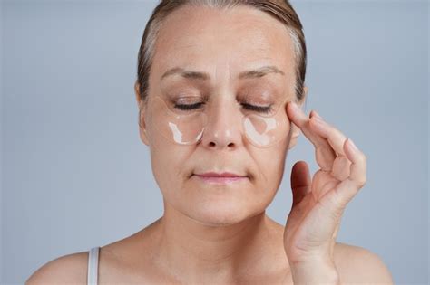 femme d âge moyen souriante aux épaules nues appliquant de la crème sur sa peau de profil sur