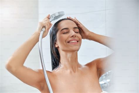 beautiful lady with closed eyes washing hair and smiling while using handheld shower head photo