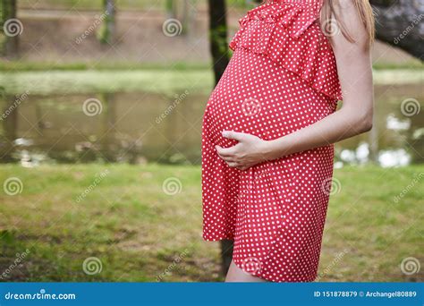 Buik Van Een Zwangere Vrouw In Rood In Een Witte Stipkleding Met Haar Die Handen Op Het Worden
