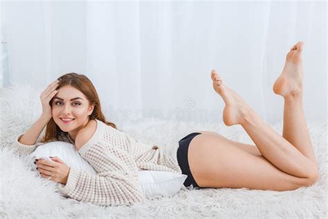 The Girl Lies On A Stomach On A Bed With Legs Upwards On A White