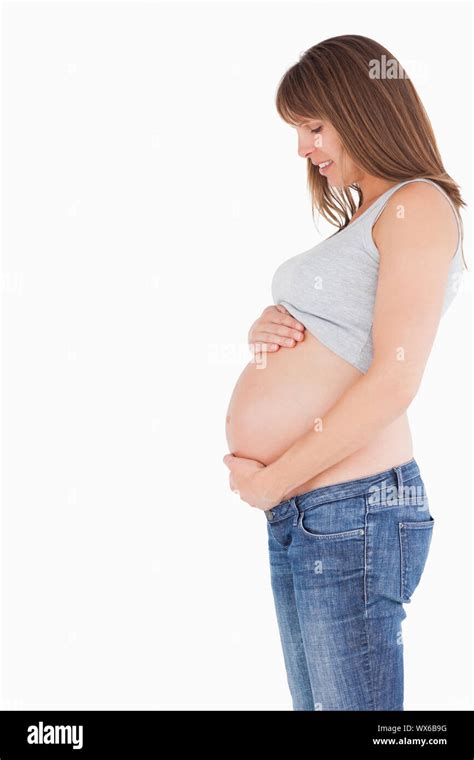 side view of an attractive pregnant woman caressing her belly while standing against a white