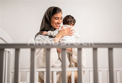 أم عربية خليجية سعودية محجبة، تحمل طفلها الرضيع بحب وحنان، إيماءات تدل على السعادة والأمان