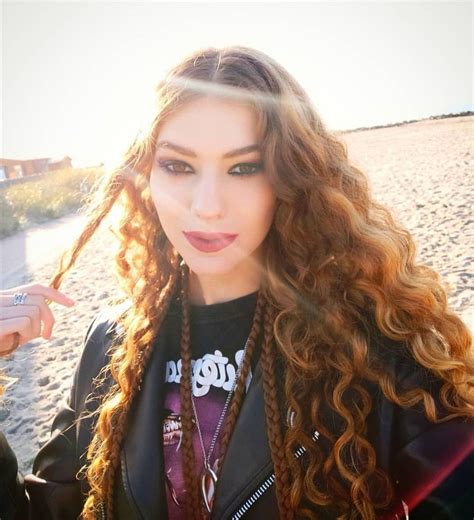 A Woman With Long Curly Hair Standing On The Beach In Front Of Sand
