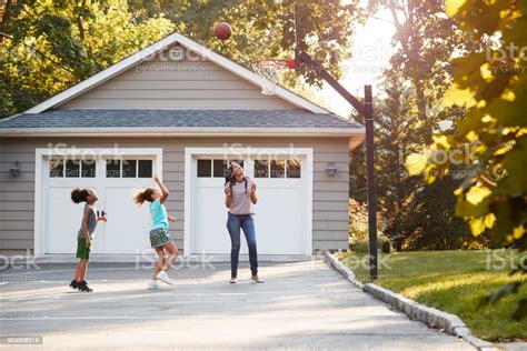 Mother And Children Playing Basketball On Driveway At Home Stock Photo