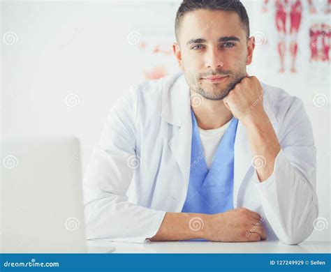 Portrait Of A Male Doctor With Laptop Sitting At Desk In Medical Office