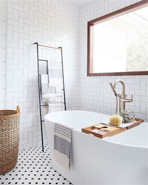 A White Bath Tub Sitting Under A Window Next To A Sink And Towel Rack