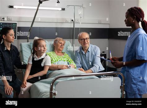 African American Nurse Discussing Sickness Symptoms With Elderly Sick Senior Woman In Hospital