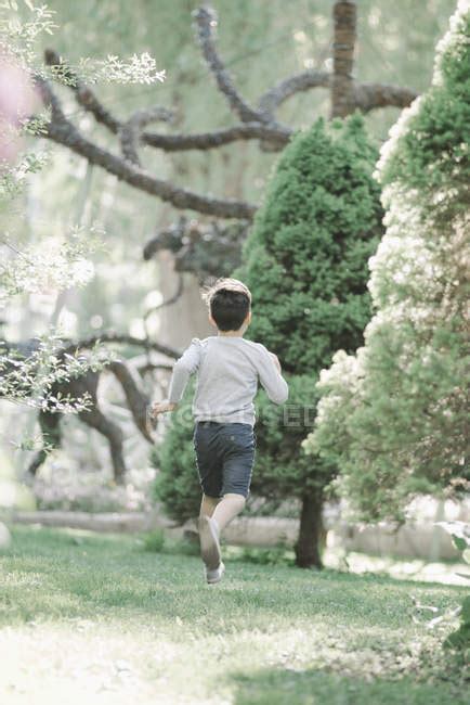 Rear View Of Elementary Age Boy Running Across Lawn In Garden — Pre