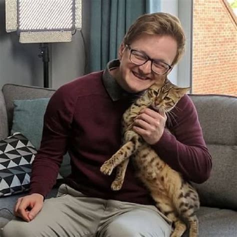 A Man Sitting On A Couch Holding A Cat