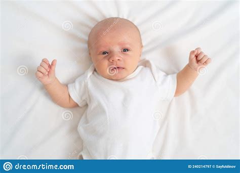 A Newborn Baby Cries On A White Sheet Childish Tantrums Top View