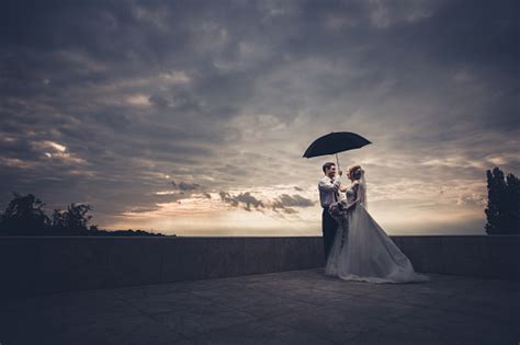 Romantic Newlywed Couple Standing Under Umbrella On A Terrace Stock