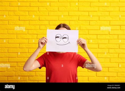 Woman hiding behind sheet of paper with smirking face near yellow brick