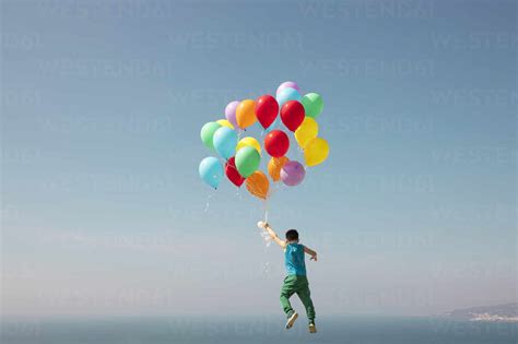 Boy Flying With Bunch Of Balloons In Sky Stock Photo