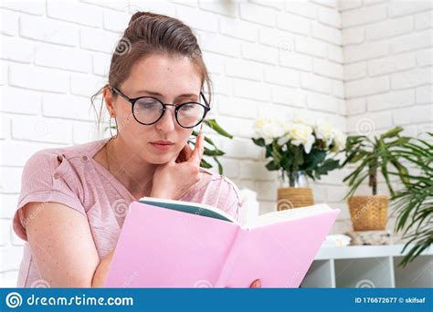 Thoughtful Woman With Glasses Is Sitting On Bed Holding A Book Read