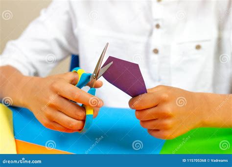 Child Hands Cutting Colored Paper With Scissors At The Table Stock