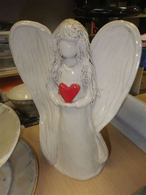 An Angel Figurine Holding A Red Heart On Top Of A Table