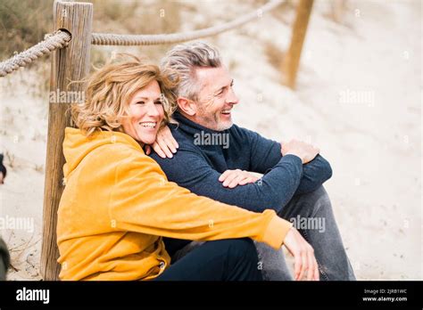 Happy Mature Woman With Man Sitting At Beach Stock Photo Alamy