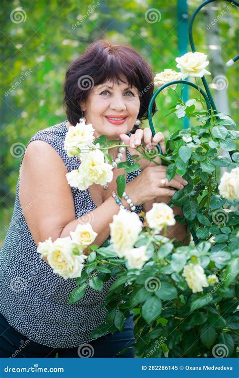 66 Year Old Woman In The Garden A Mature Woman Enjoys The Flowers Of A