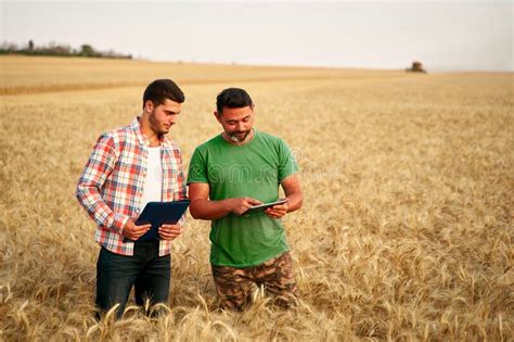 Two Farmers Stand In Wheat Stubble Field Discuss Harvest Crops