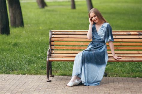 Beautiful Girl Sitting On A Bench Brunette In A Bright Dress Sunny