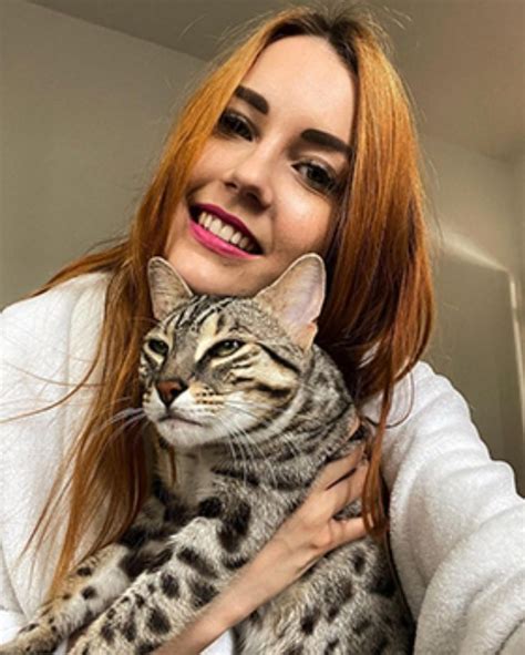 A Woman Holding A Cat In Her Arms And Looking At The Camera With An Intense Smile On Her Face
