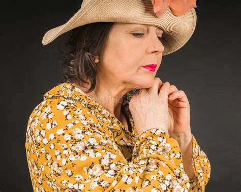 Portrait Of A Pensive Mature Woman In A Straw Hat And Yellow Dress With A Floral Pattern On A