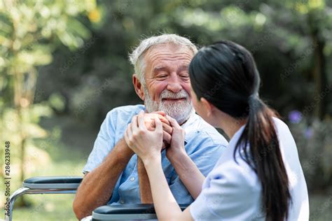 Caring Nurse With Senior Man Sitting On Wheelchair In Gaden Asian Woman Caucasian Man Asking