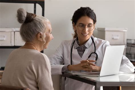 Female Doctor And Mature Patient Use Laptop At Consultation Stock Image