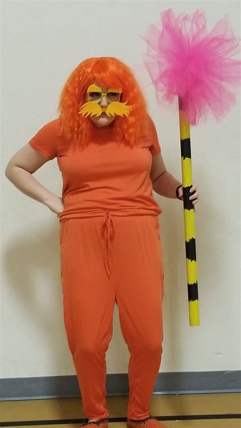 A Woman In An Orange Jumpsuit Holding A Broom And Wearing A Fake Moustache