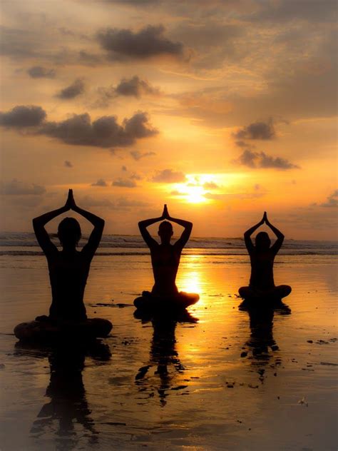Three People Sitting On The Beach Doing Yoga Exercises At Sunset With