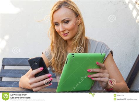 sensual happy blonde woman sitting on wooden bench she is using mobile phone and tablet pc