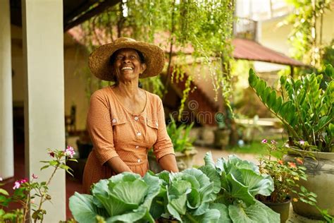Senior Indian Female Farmer In Straw Hat In Garden Taking Care Of