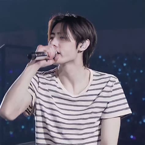 A Male In A Striped Shirt Is Singing Into A Microphone