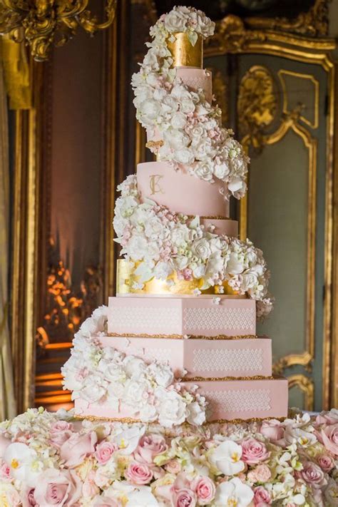 a pink and white wedding cake with flowers on the bottom tier is surrounded by gold framed mirrors