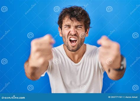 Hispanic Young Man Standing Over Blue Background Angry And Mad Raising