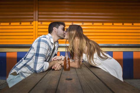 romantic couple having a good time kissing by picnic table in amusement park — happy female