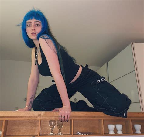 A Woman With Blue Hair Standing On Top Of A Wooden Counter Next To Wine