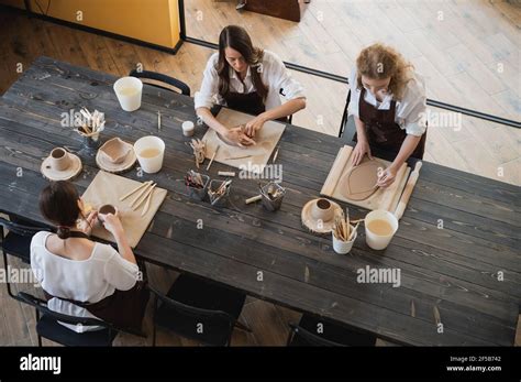 Three Women In Aprons Sitting By Table Kneading Clay And Making