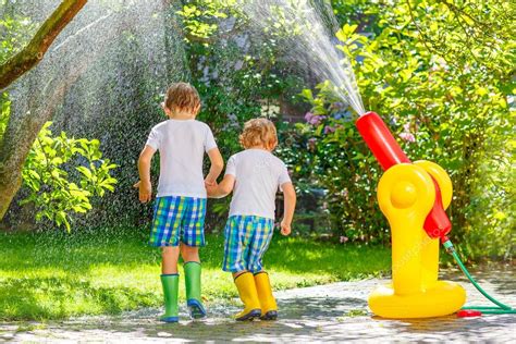 Two Little Kids Playing With Garden Hose And Water In Summer Stock